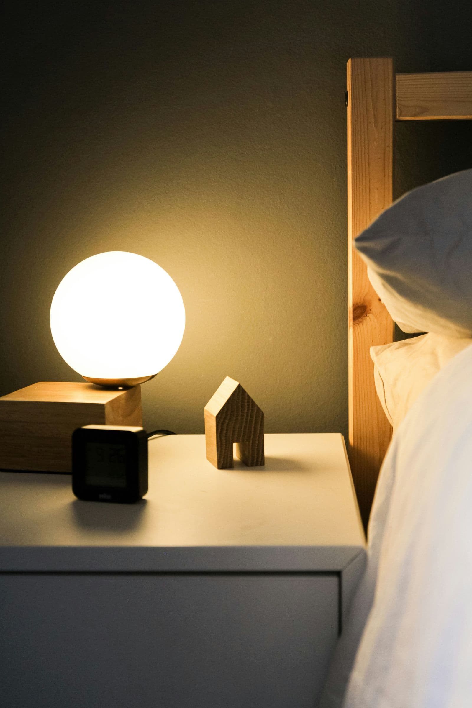 Nattbord med vekkerklokke og lampe ved siden av en seng